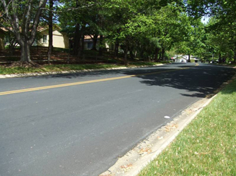 Photo shows the same street looking to the right.  It is lined with trees on both sides and houses on the left.  The road is going slightly uphill and disappears about 200 feet away.